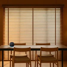 Dining room featuring two chairs and table in front of wooden blinds, creating a warm ambient lighting effect.
